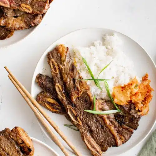 White plate with two grilled kalabi with a side of kimchi and white rice.