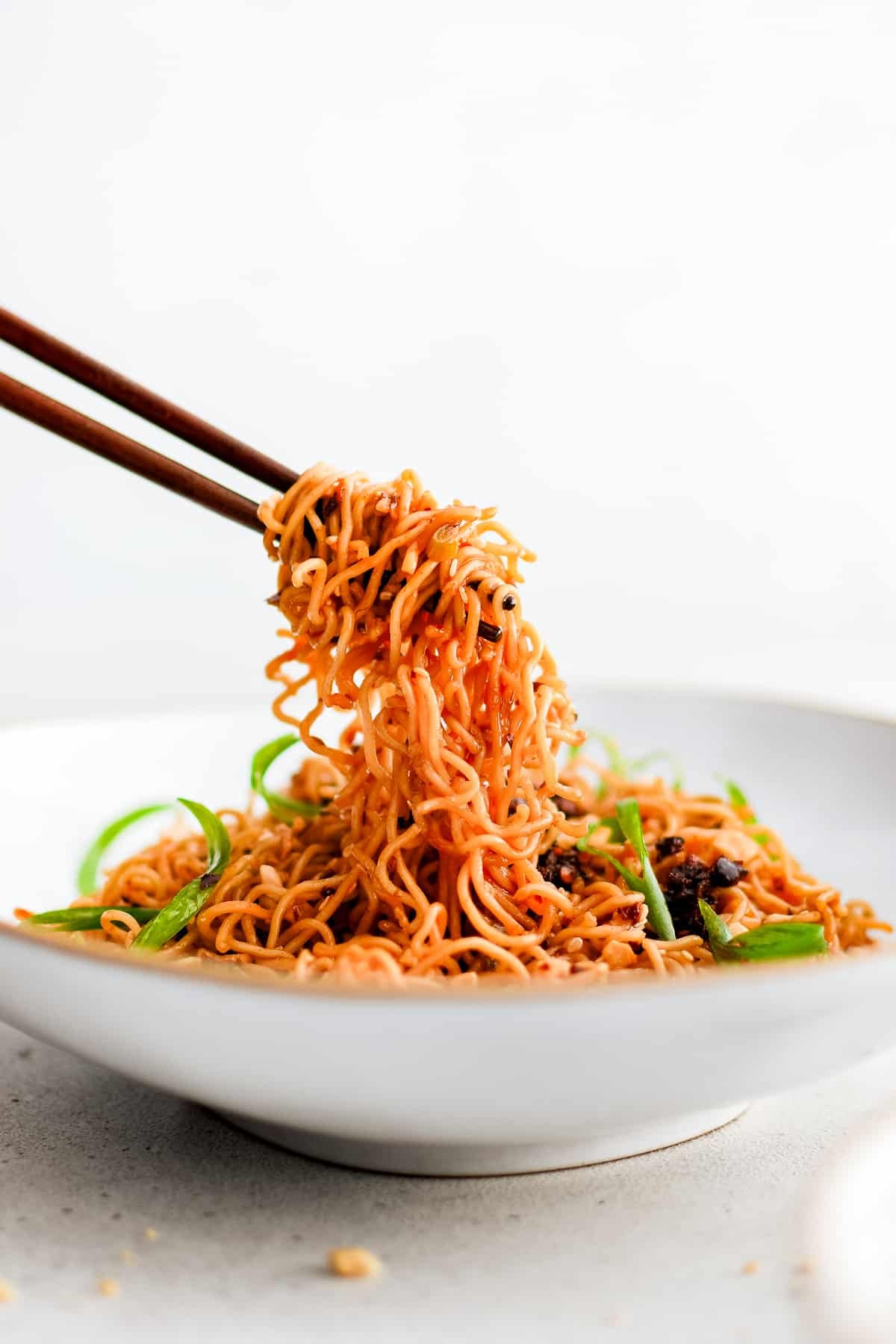 Chopsticks scooping a generous mouthful of spicy ramen noodles from a large, shallow serving bowl.