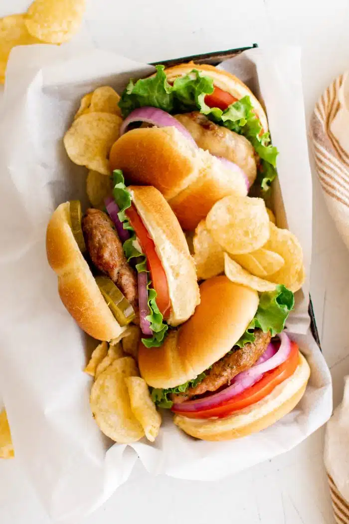 Looking down at a small tray filled with three cooked turkey burgers on buns with lettuce, tomato, onion, pickles, and cheese.