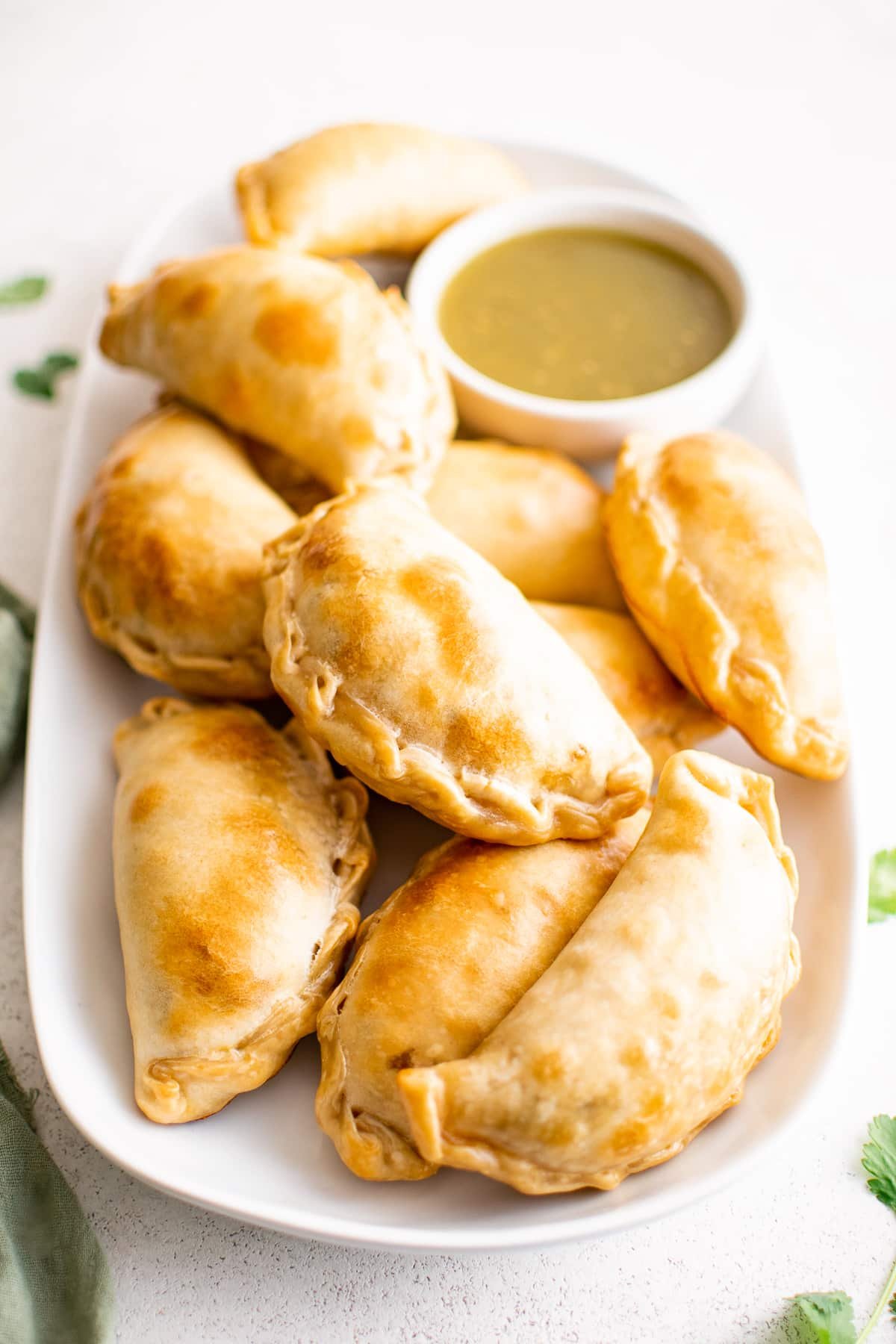 A large oval plate piled with golden baked beef empanadas.