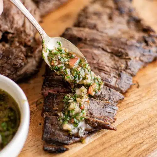 Spooning chimichurri sauce over grilled marinated flank steak.