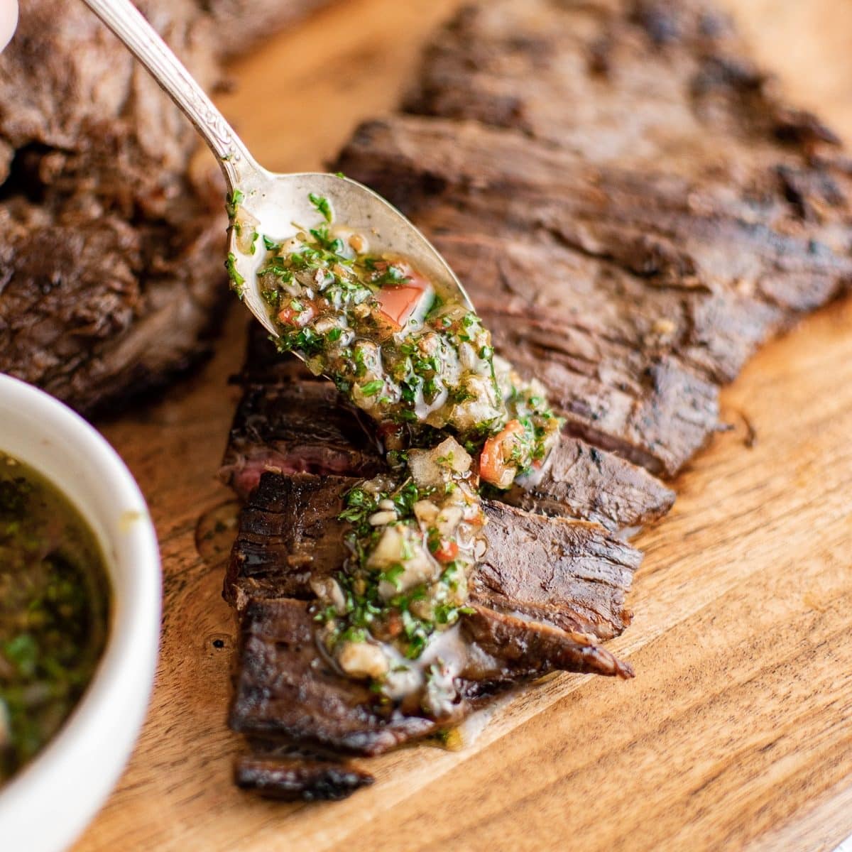 Spooning chimichurri sauce over grilled marinated flank steak.