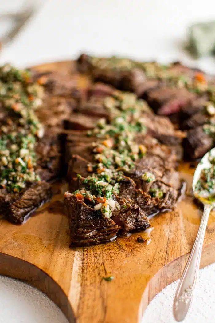 Thinly sliced marinated flank steak on a wooden cutting board topped with chimichurri sauce.