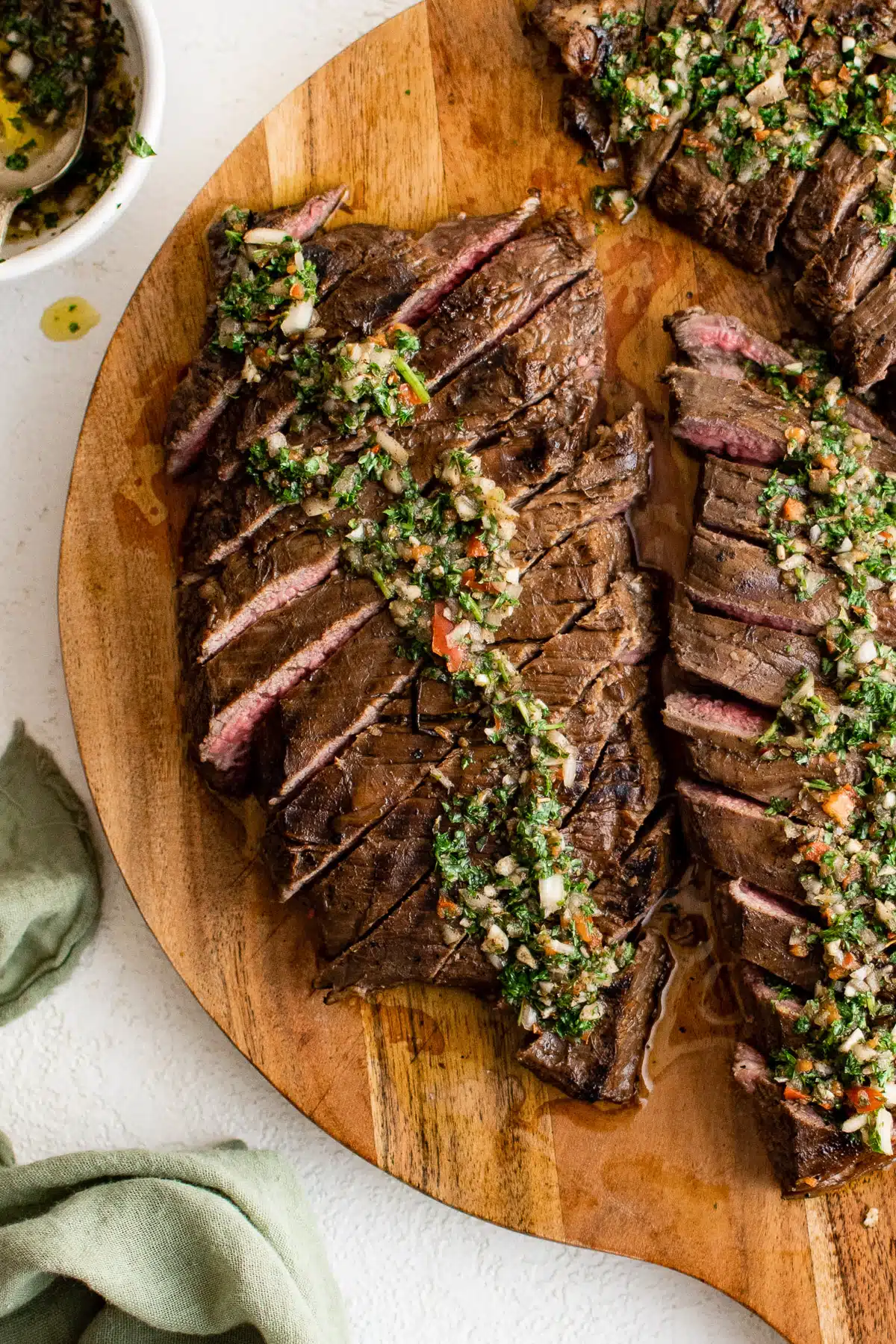 Thinly sliced marinated flank steak on a wooden cutting board topped with chimichurri sauce.