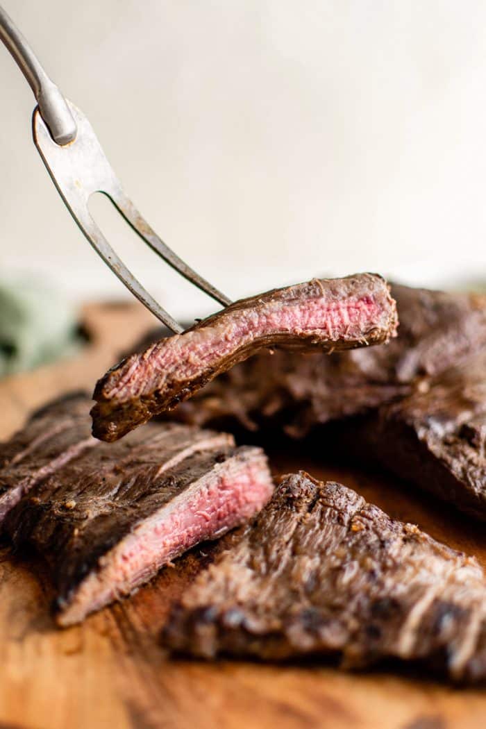 Meat fork with a slice of cooked marinated flank steak.