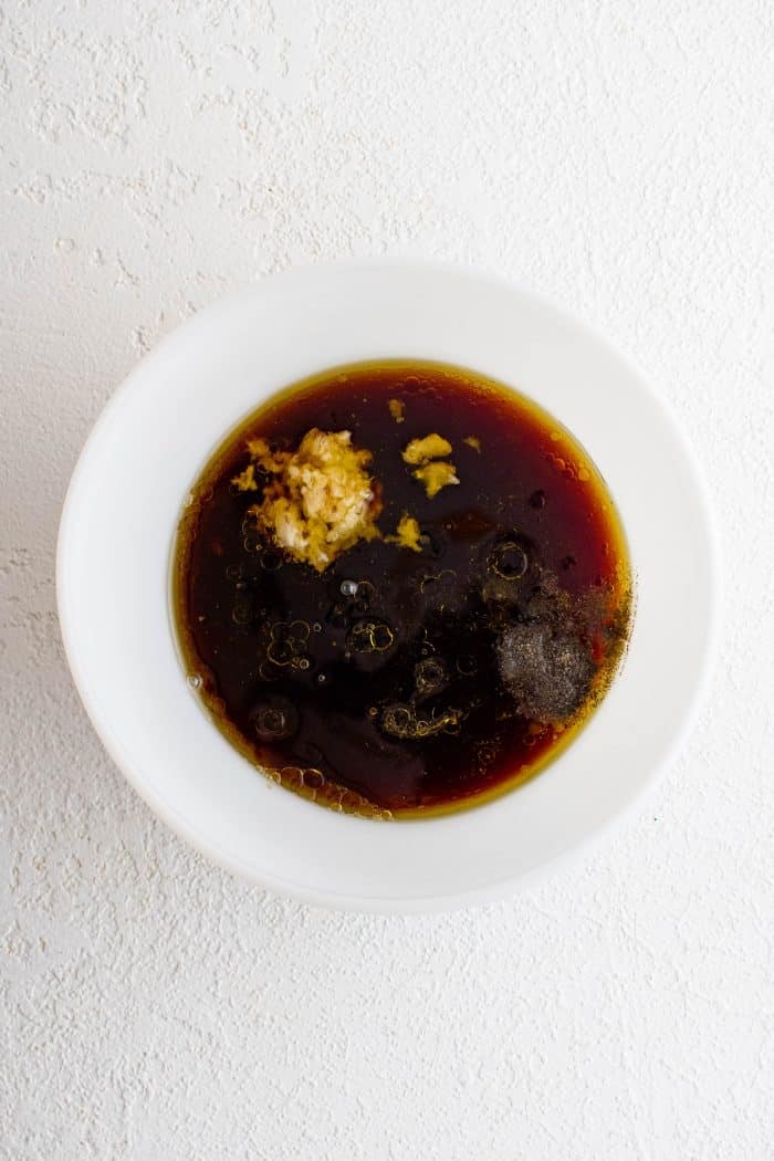 White bowl filled with red wine, soy sauce, olive oil, brown sugar, minced garlic, lemon juice, white wine vinegar, salt, and black pepper.
