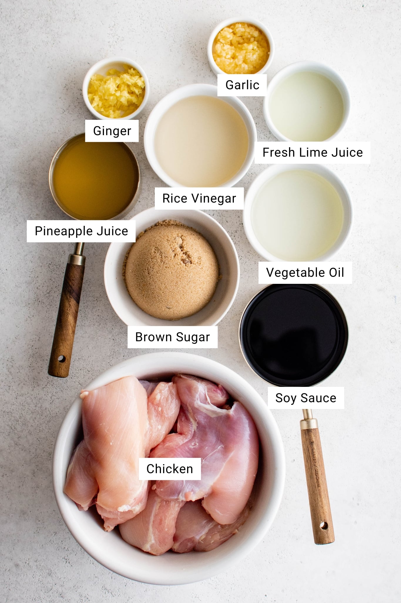 Overhead view of Hawaiian chicken marinade ingredients in small bowls: soy sauce, pineapple juice, brown sugar, rice vinegar, vegetable oil, lime juice, garlic, ginger, and raw chicken.