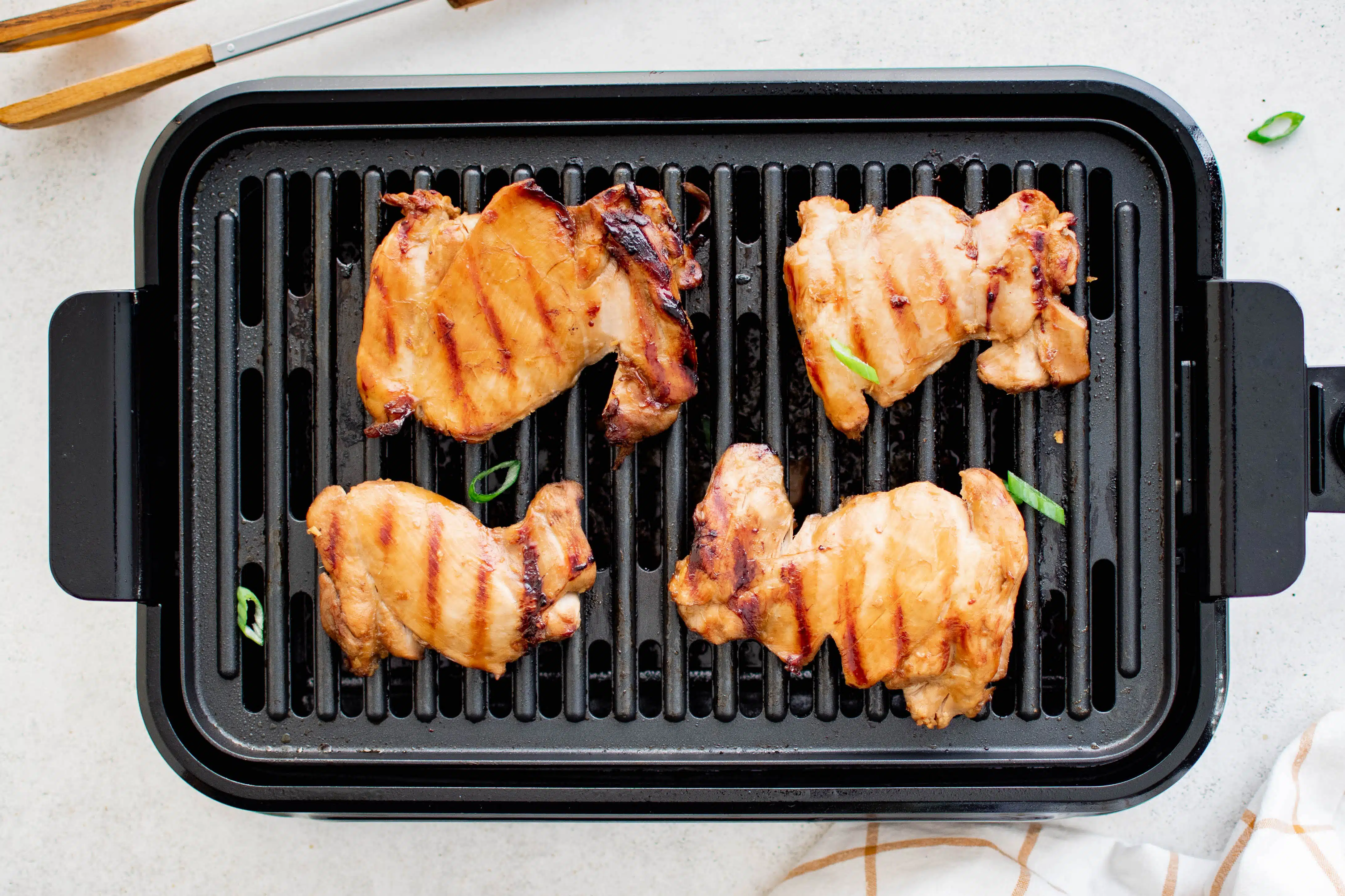 Four marinated boneless skinless chicken thighs cooking on an indoor electric grill.