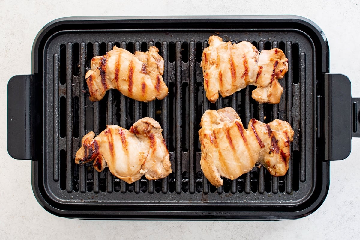 Four marinated chicken thighs grilling on a stovetop grill pan with visible sear marks.