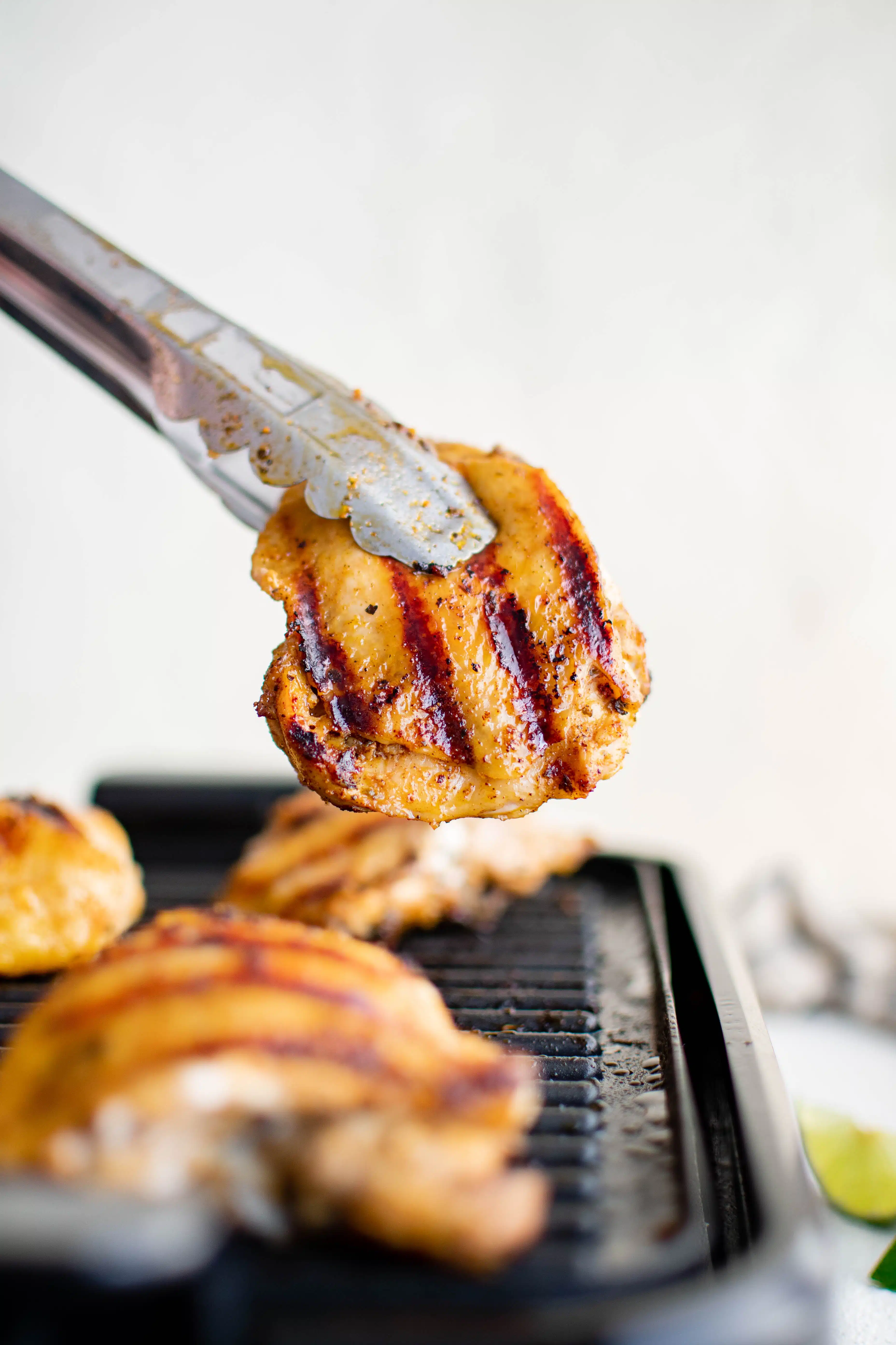 Metal tongs removing grilled pollo asado from an indoor electric grill.