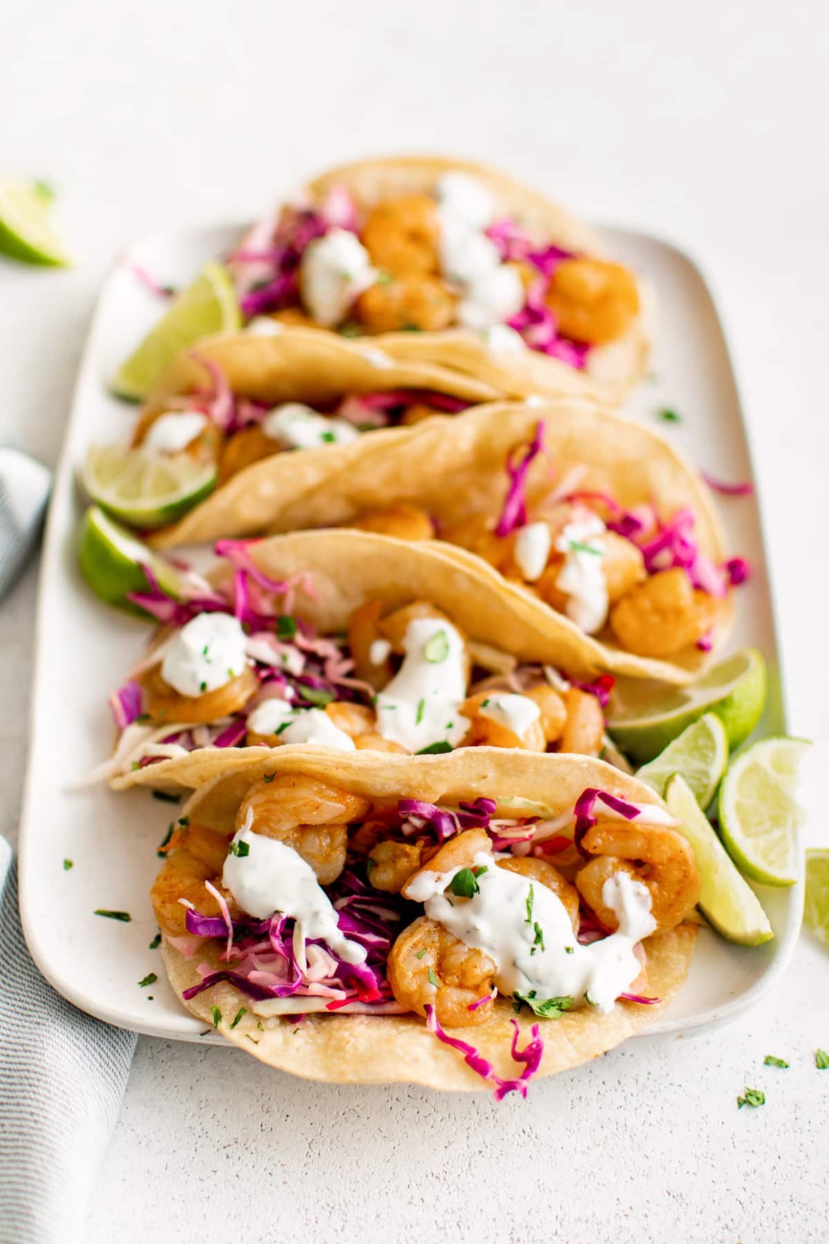Large white rectangle plate topped with five assembled shrimp tacos filled with cabbage slow, shrimp, and creamy taco sauce.