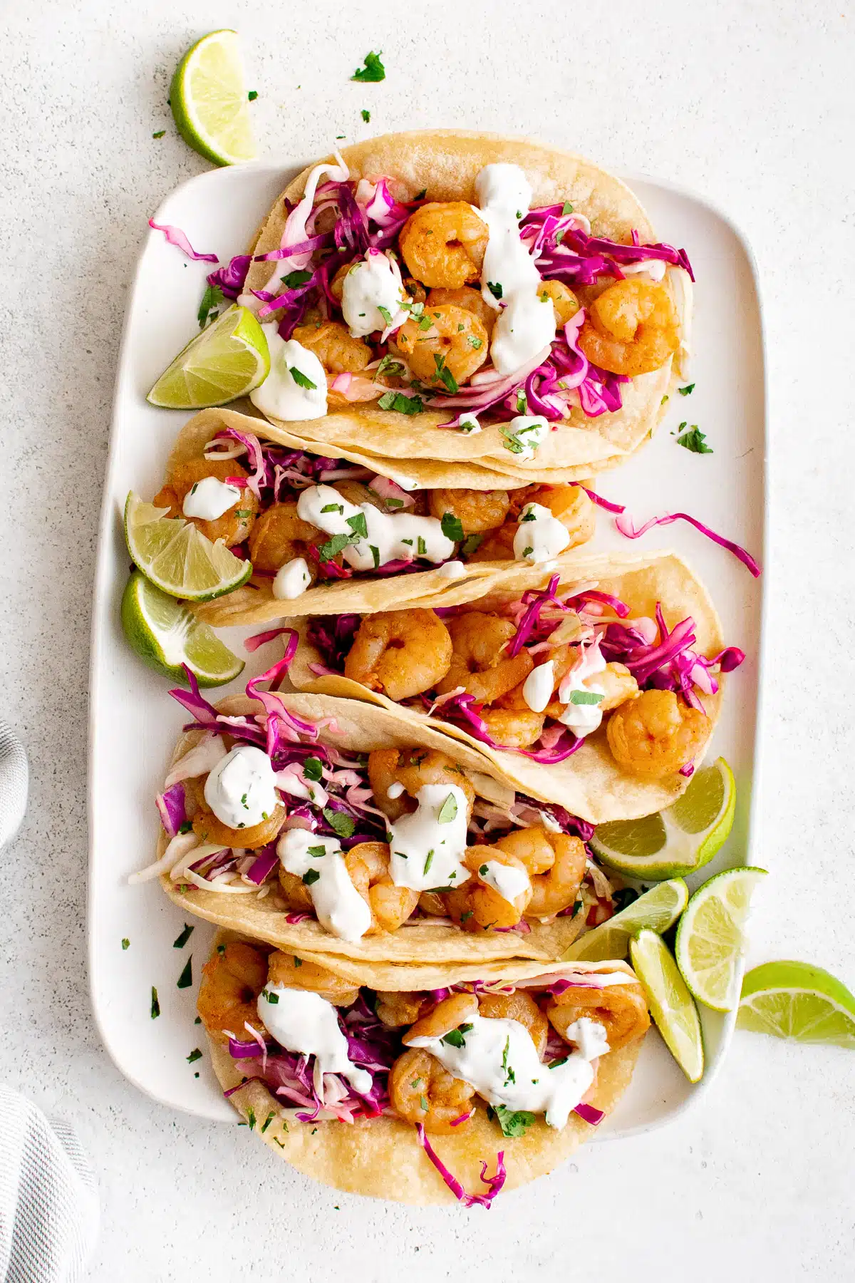 Large white rectangle plate topped with five assembled shrimp tacos filled with cabbage slow, shrimp, and creamy taco sauce.