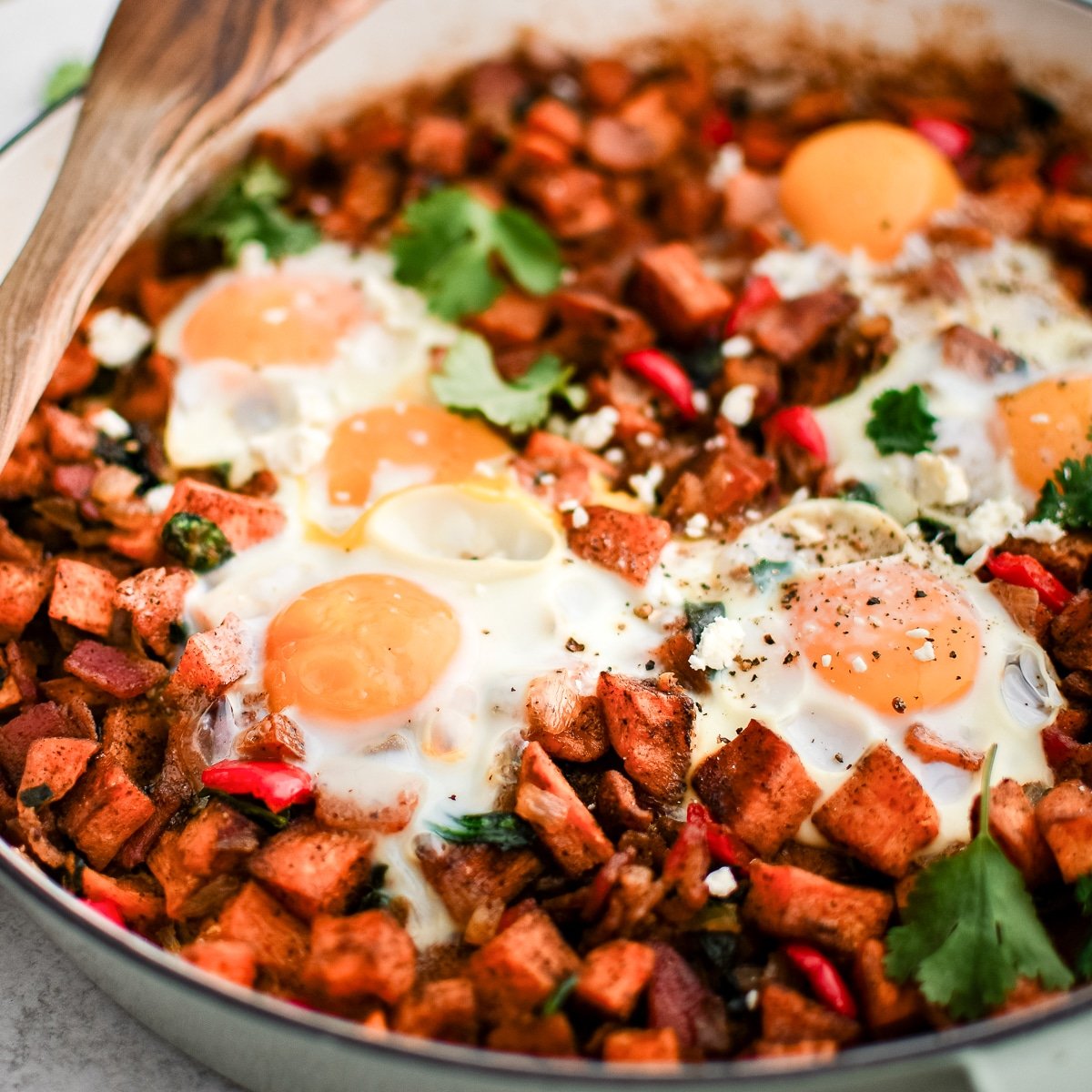 Large skillet filled with roasted sweet potatoes, bacon, and sauteed veggies and topped with eggs and fresh cilantro.