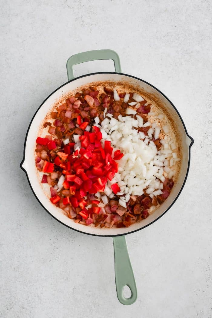 Diced red bell pepper and onion added to a large skillet with crispy cooked bacon pieces.