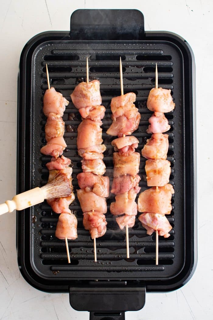 Four chicken skewers cooking on an indoor electric grill.