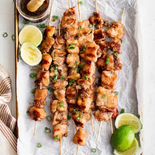 Baking sheet linked with parchment paper and topped with a stack of cooked chicken Yakitori skewers.
