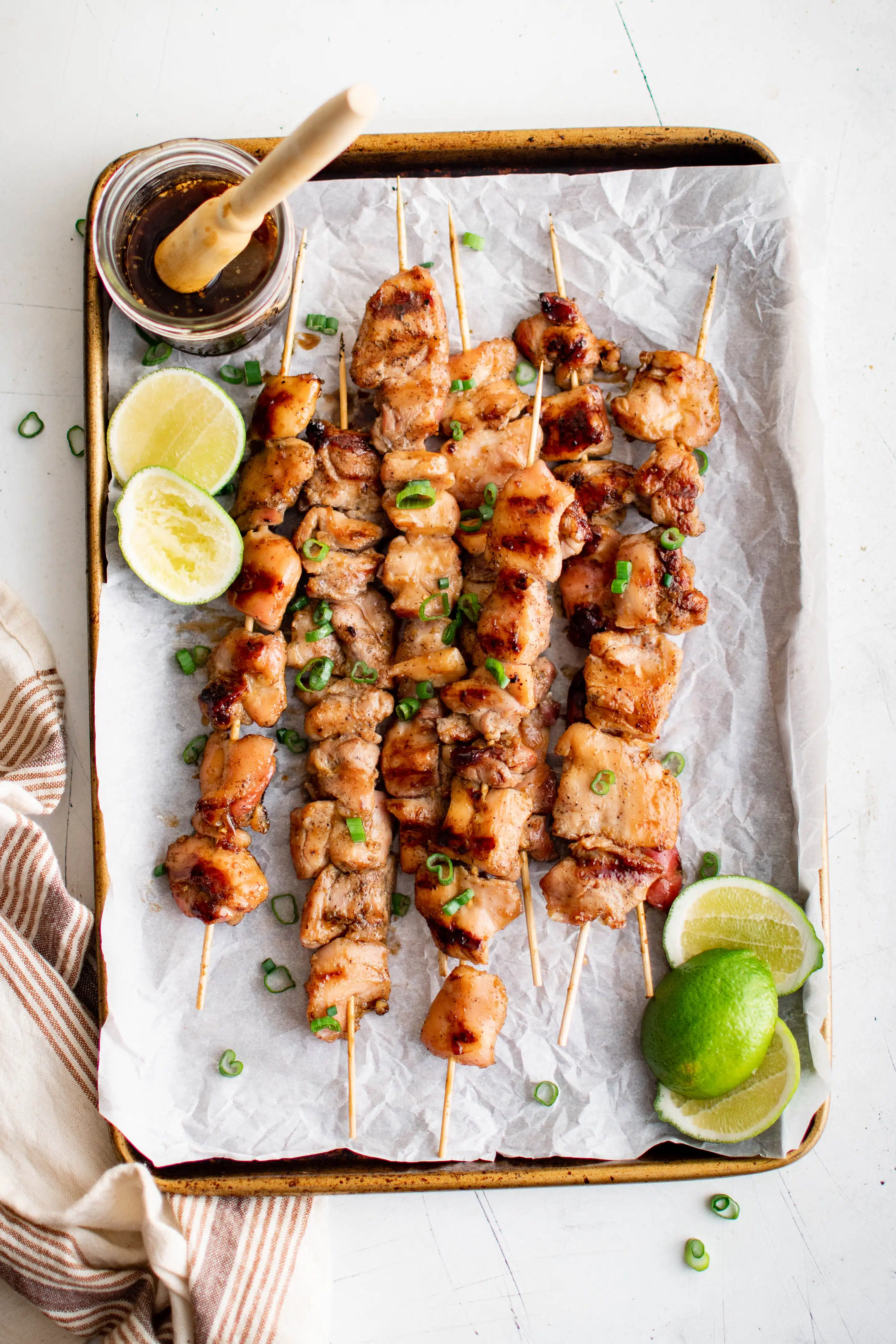 Baking sheet linked with parchment paper and topped with a stack of cooked chicken Yakitori skewers.