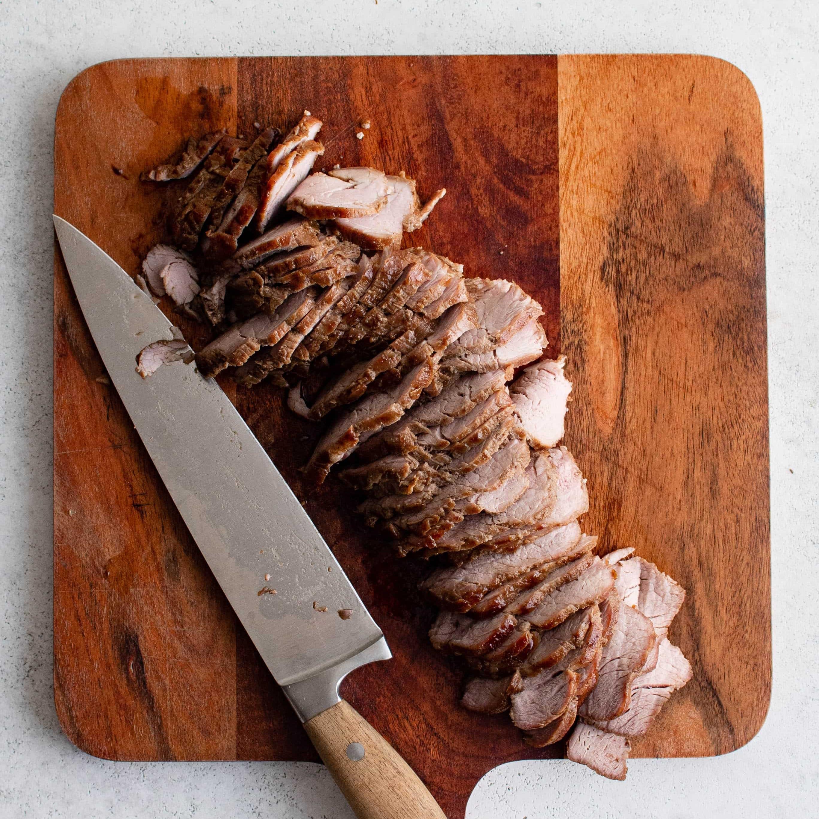 Thinly sliced pork tenderloin on a wood cutting board.