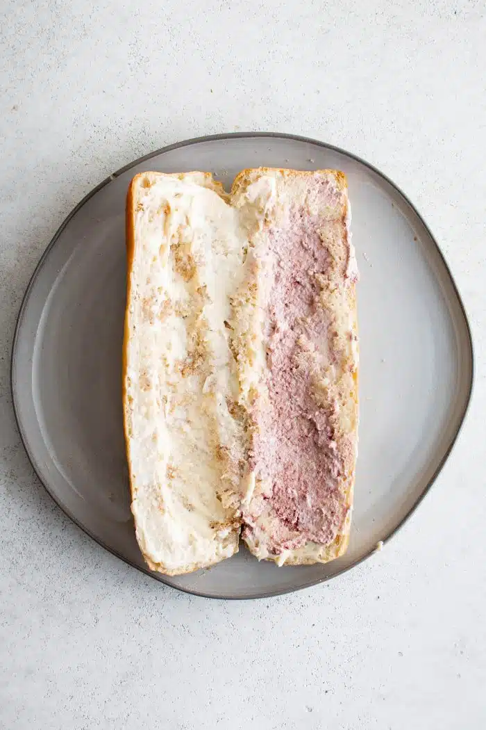 One French baguette on a plate cut in half lengthwise with pate spread on top of the mayonnaise.