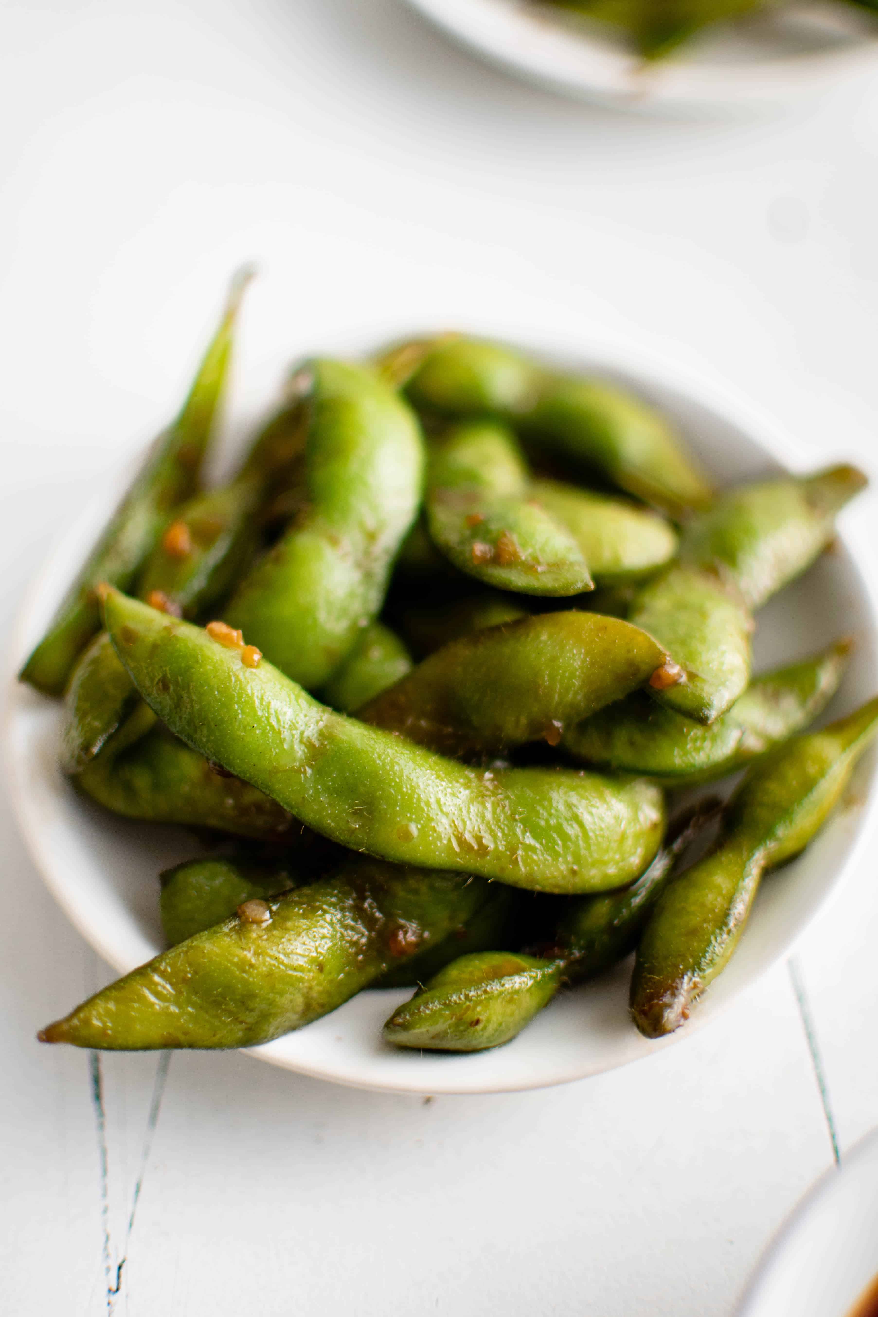 Small white serving dish filled with cooked edamame seasoned with soy sauce, garlic, sugar, and salt.