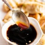 Spoon dipped in a small white ramekin filled with gyoza sauce.