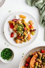 White dinner plate with white rice topped with Hunan chicken stir fry made with chicken and vegetables coated in sweet and sour sauce and a side of chopped green onions in a small white ramekin on the side.