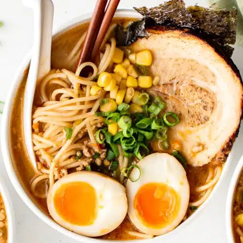 White bowl filled with miso ramen broth and ramen noodles topped with chashu pork, seaweed, ramen egg, corn, and green onions.