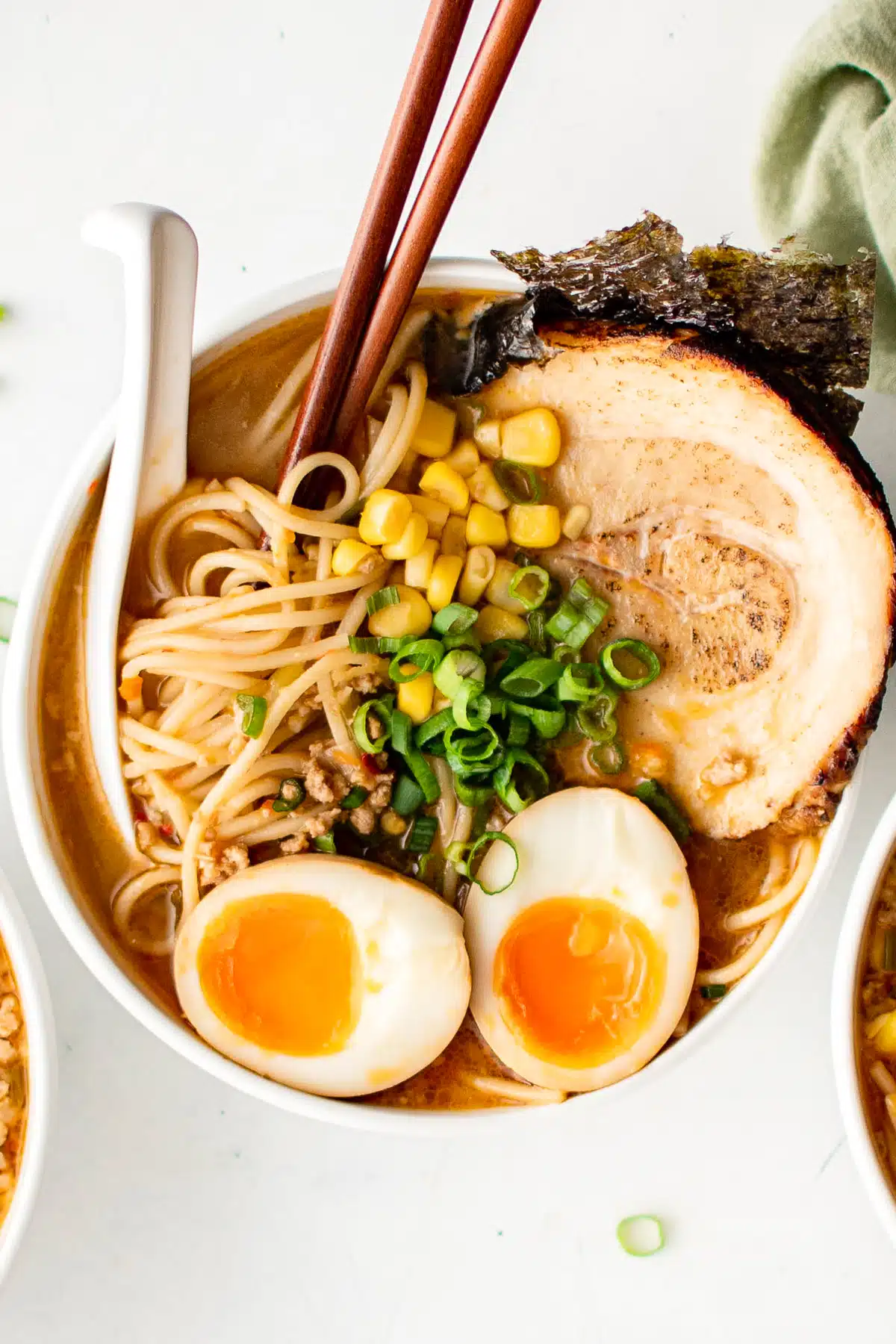 White bowl filled with miso ramen broth and ramen noodles topped with chashu pork, seaweed, ramen egg, corn, and green onions.