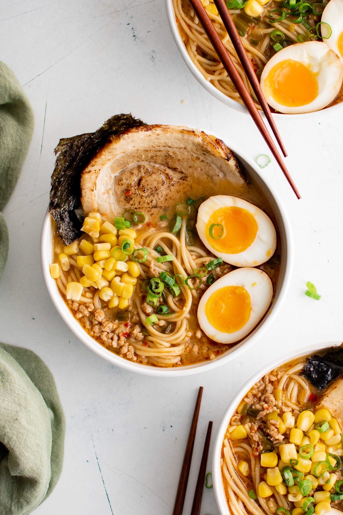 Three bowls filled with miso ramen broth and ramen noodles topped with chashu pork, seaweed, ramen egg, corn, and green onions.