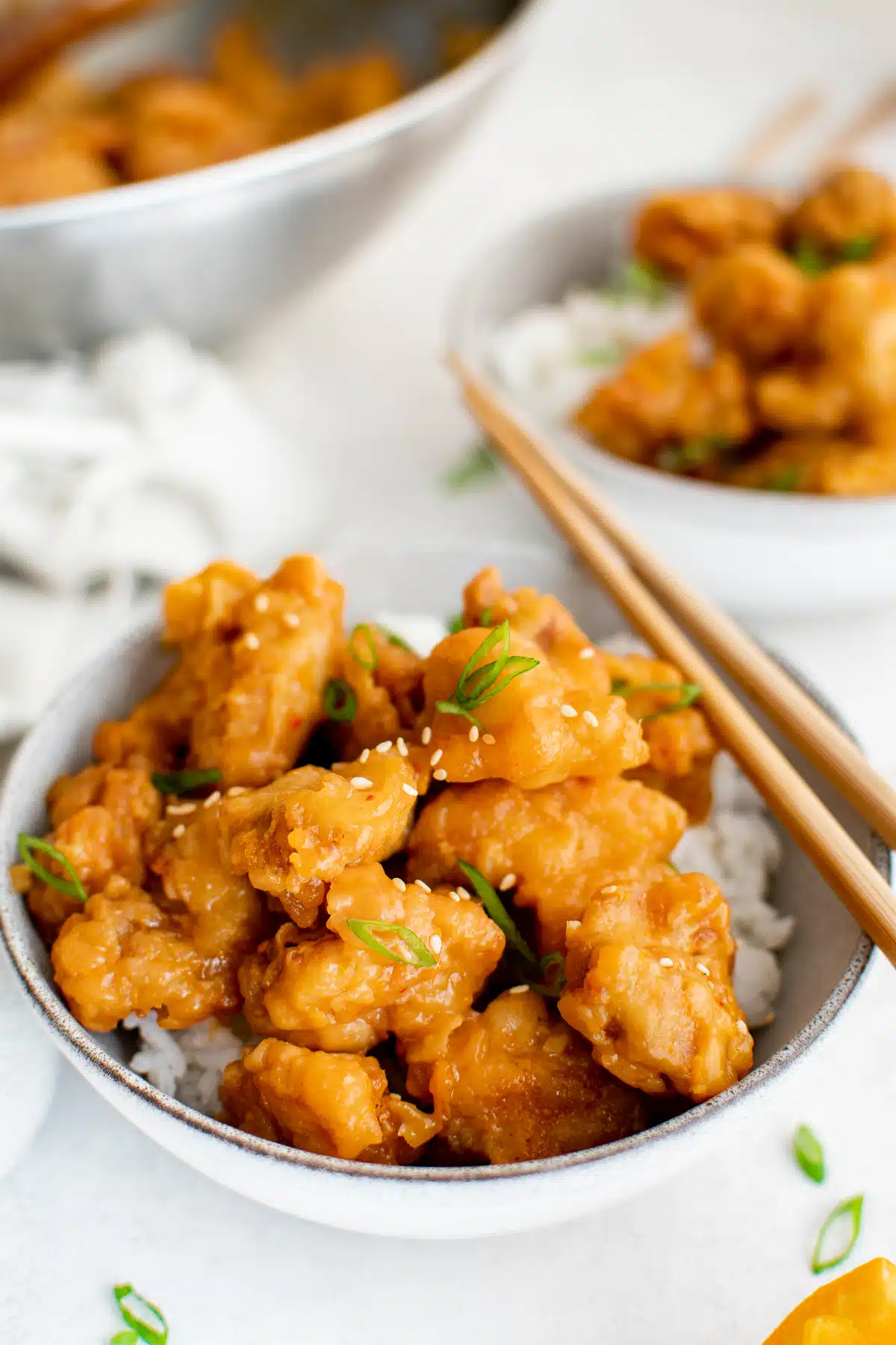 White bowl filled with white rice and topped with orange chicken pieces garnished with sliced green onions.