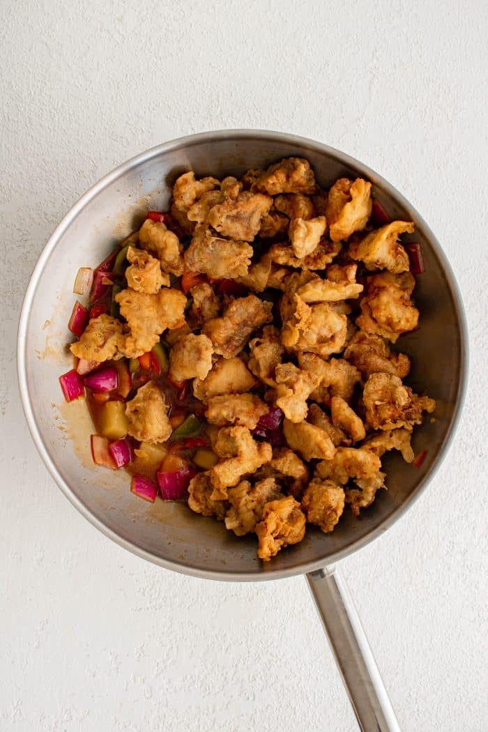 Fried chicken pieces added to a large wok filled with veggies, pineapple, and sweet and sour sauce.
