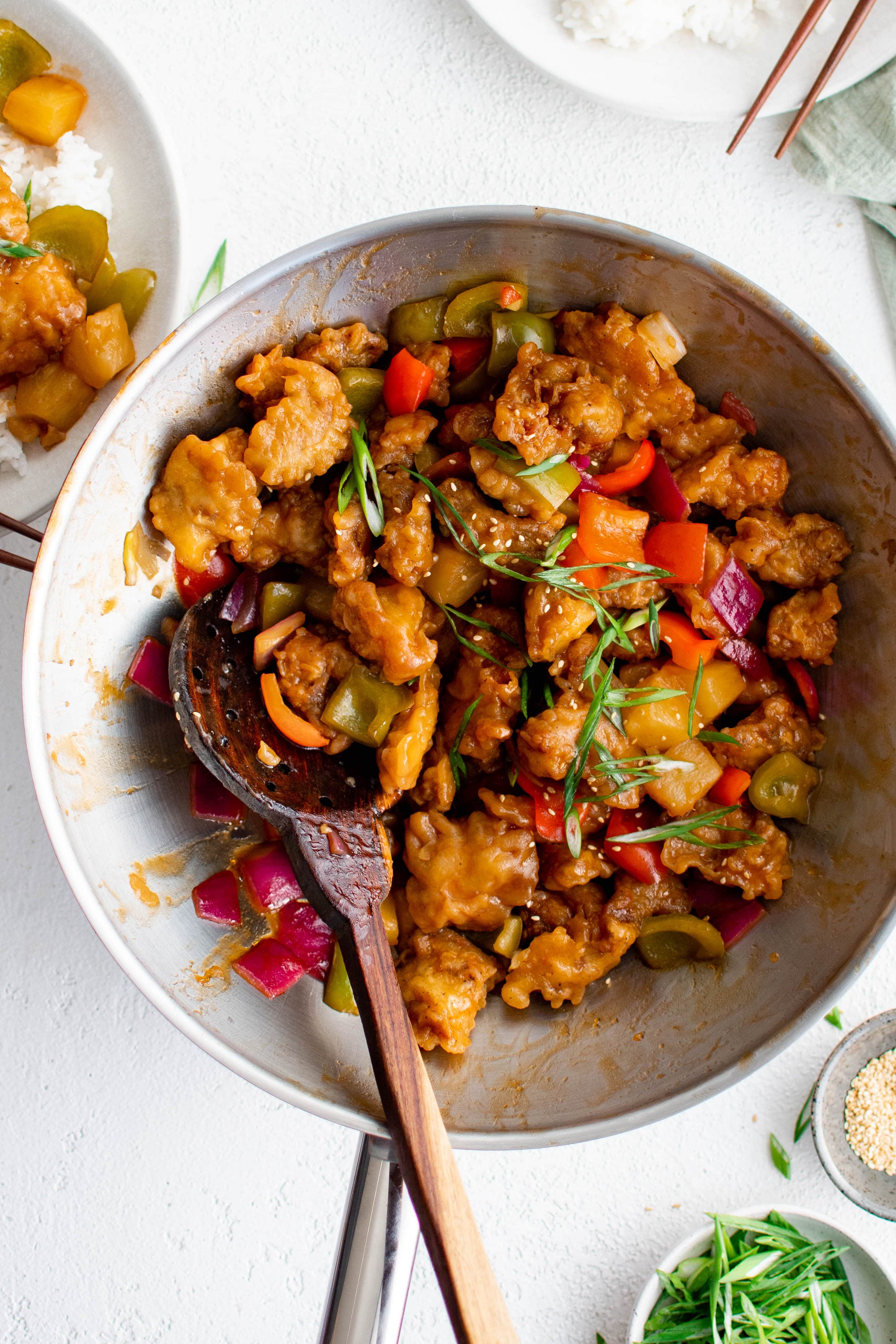 Large wok filled with vibrant sweet and sour chicken with bell peppers and pineapple.