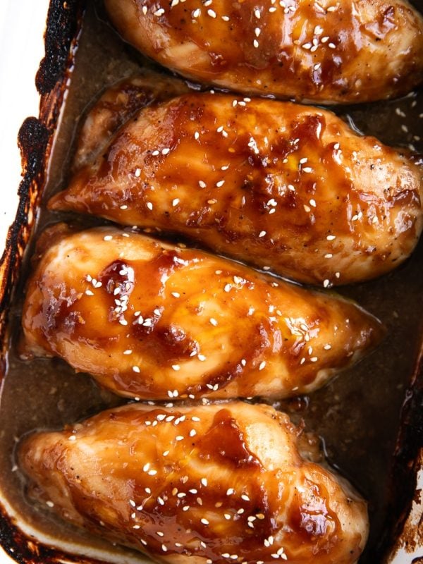 Four large baked chicken breasts coated in homemade teriyaki sauce and sprinkled with sesame seeds.