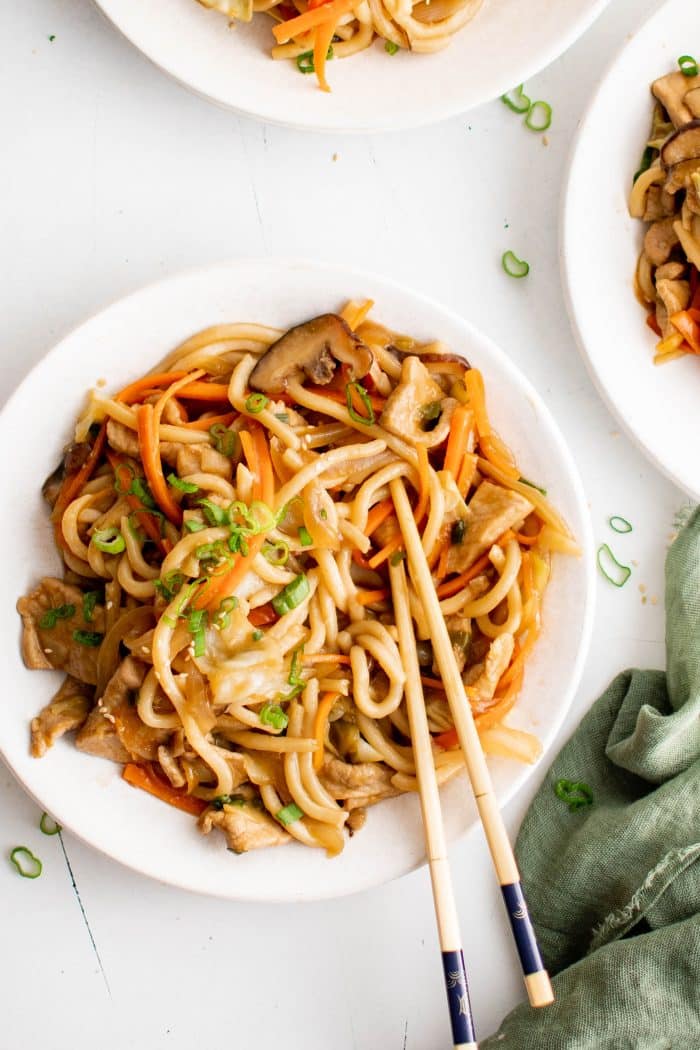 White plate filled with yaki udon noodles made with thinly sliced pork, mushrooms, carrots, and cabbage and garnished with green onions.