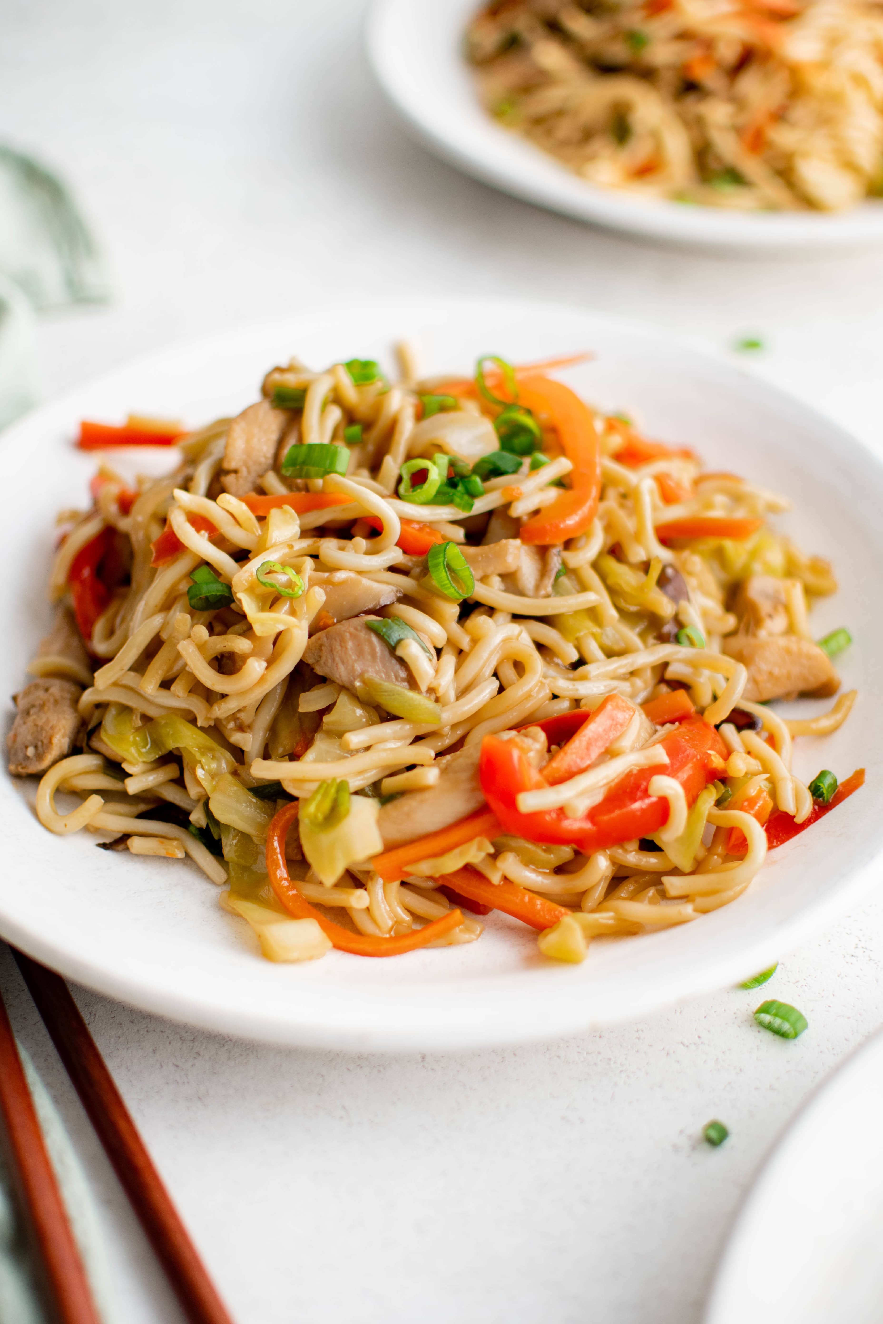 White plate filled with yakisoba noodles filled with vegetables and chicken.