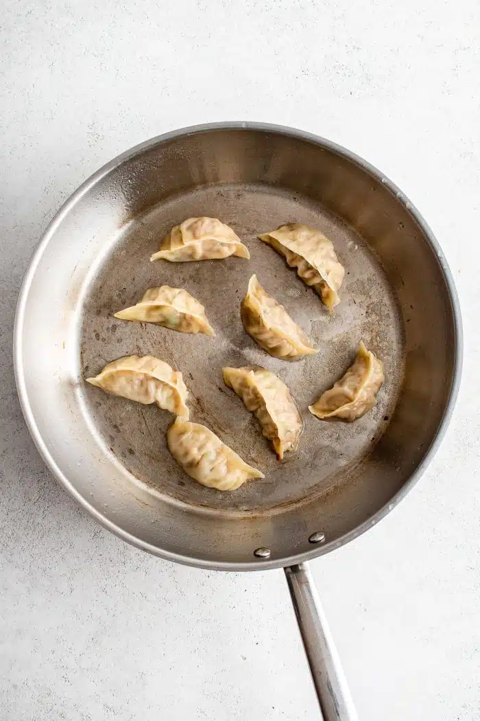 Large stainless steel skillet filled with eight pork gyoza.