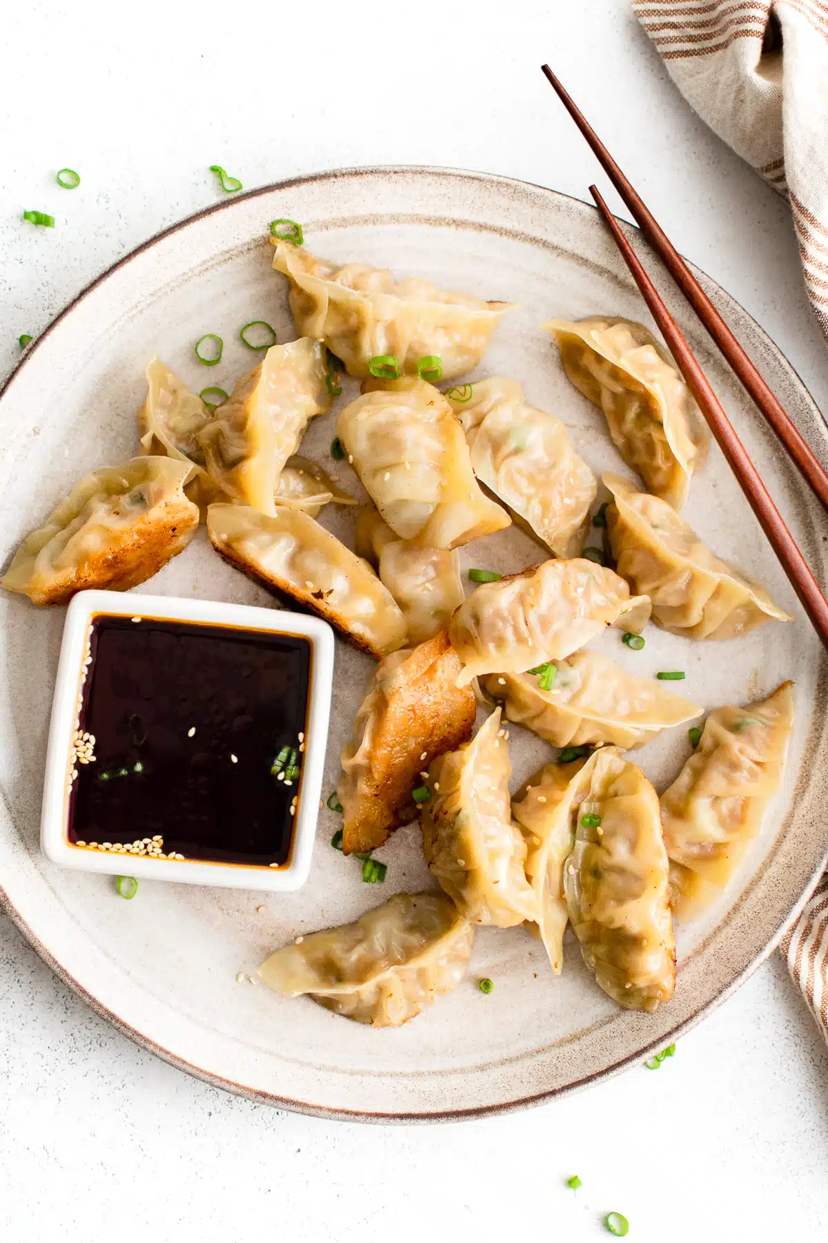 Large plate filled with golden pan-fried pork gyoza served with a side of gyoza dipping sauce.