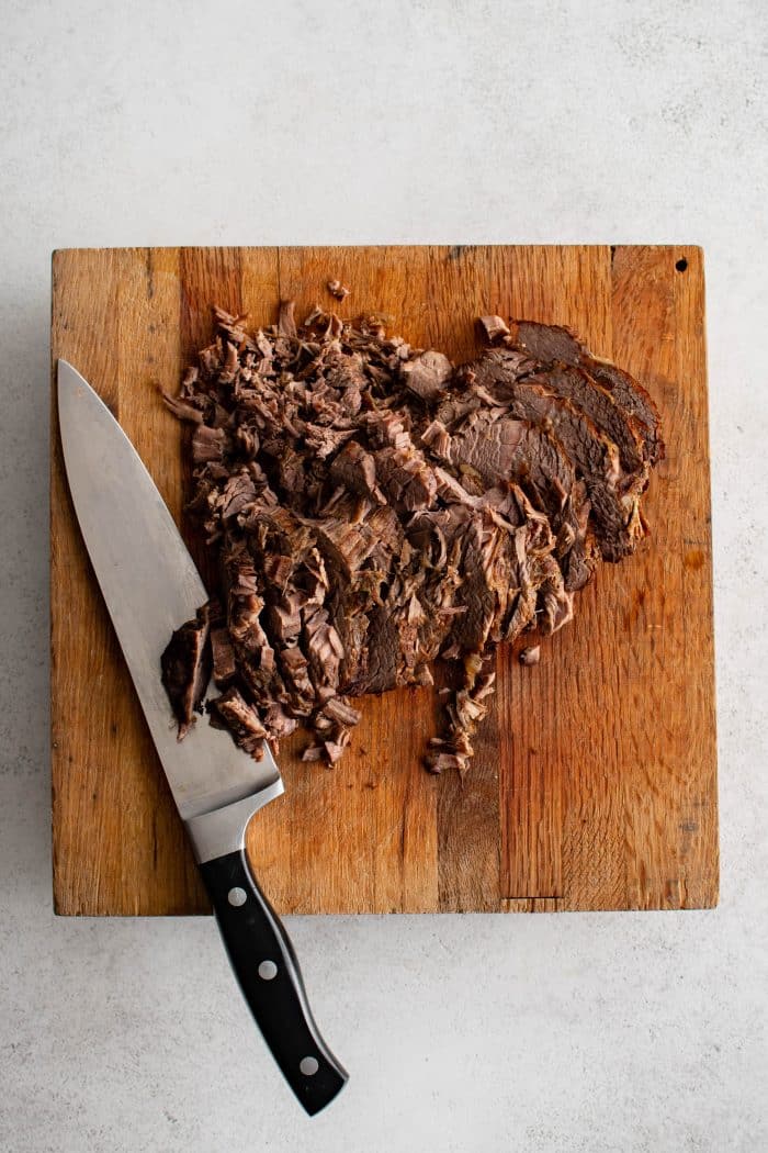 Thinly sliced cooked chuck roast on a large wood cutting board.