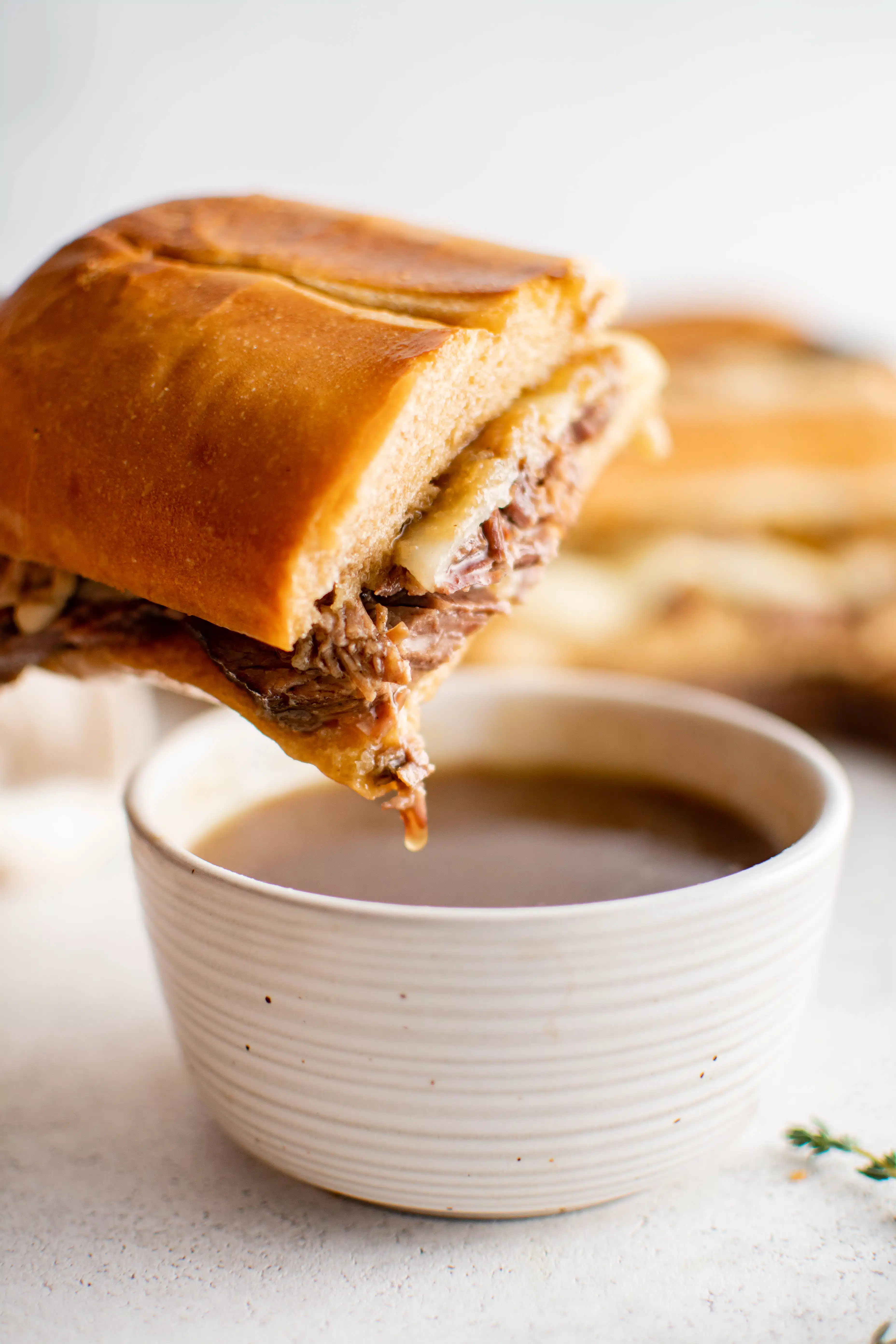 Half of a French dip sandwich dipped into a bowl filled with au jus.