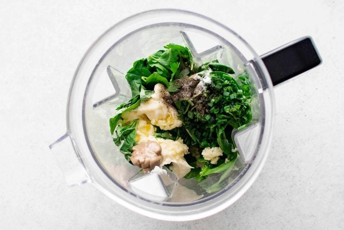 All of the ingredients needed to make homemade green goddess dressing in the bowl of a blender.