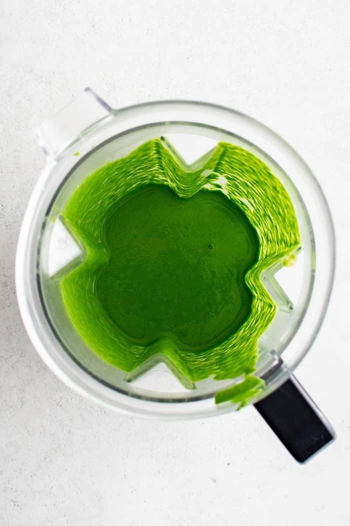 Beautiful emerald colored homemade green goddess dressing in the bowl of a blender.