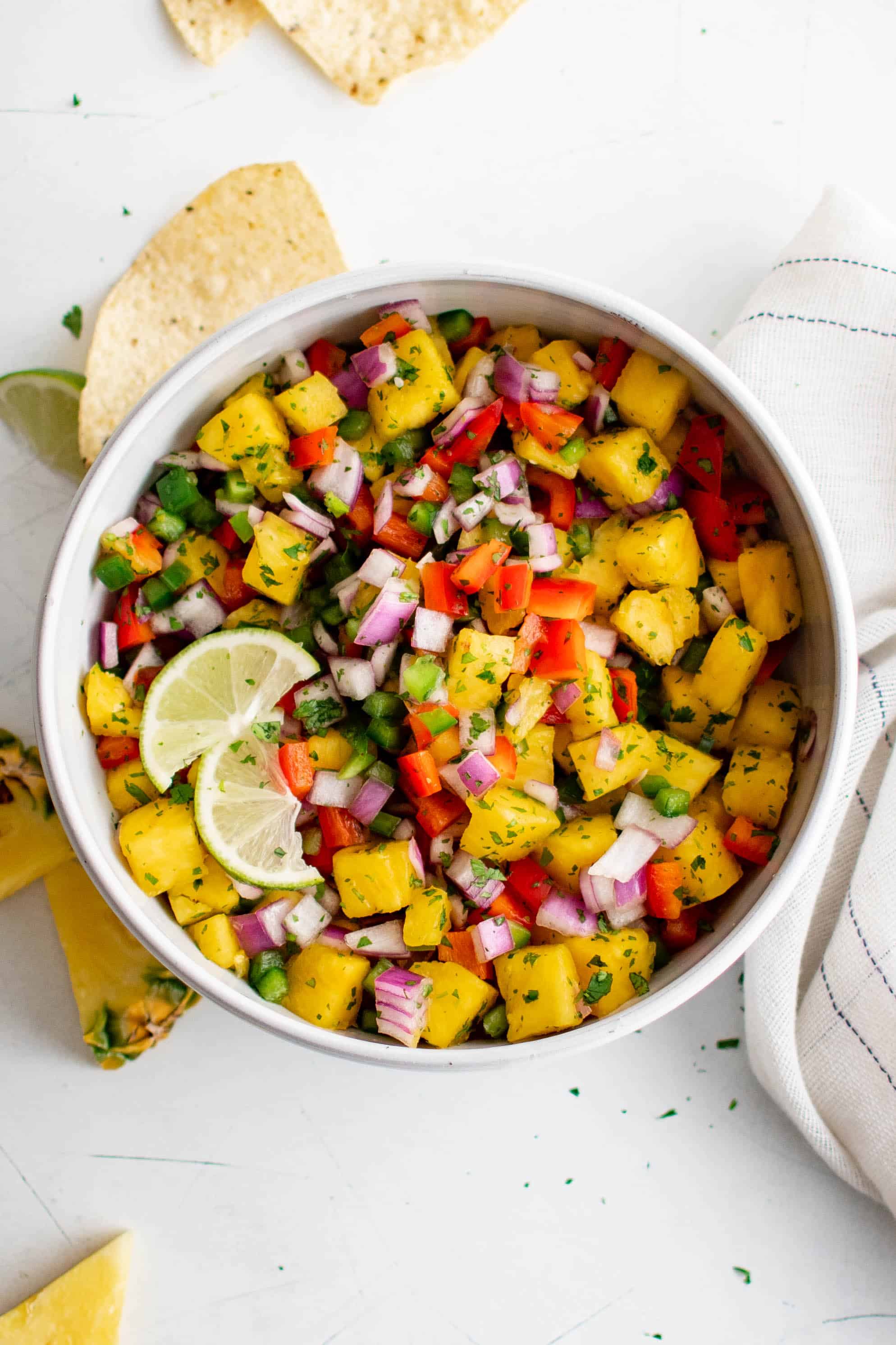 Overhead image of a large white bowl filled with fresh pineapple salsa made with diced red onion, red bell pepper, jalapeno, and pineapple and mixed with fresh lime juice, pineapple juice, and minced cilantro.