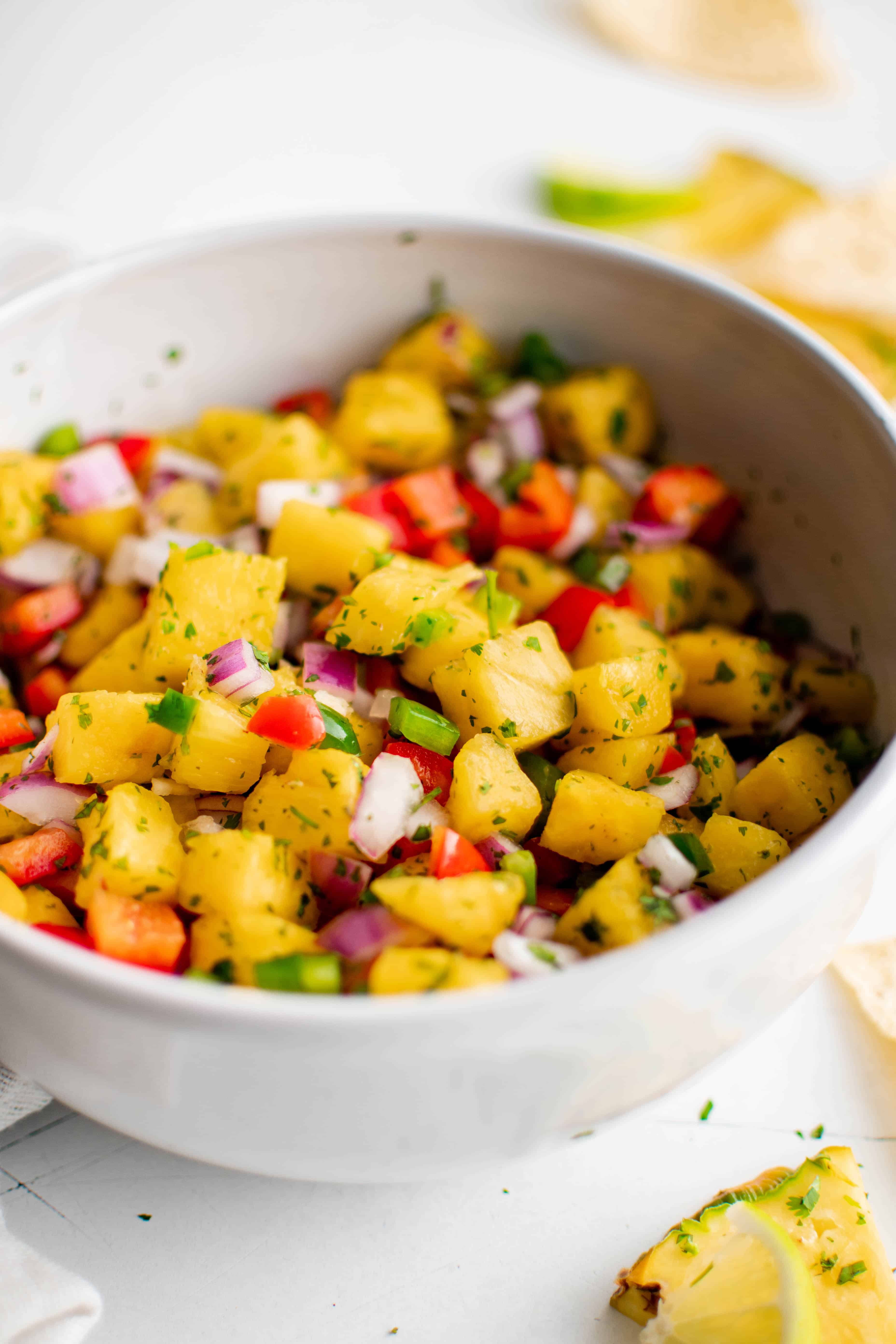 Close up of a large white bowl filled with fresh pineapple salsa made with diced red onion, red bell pepper, jalapeno, and pineapple and mixed with fresh lime juice, pineapple juice, and minced cilantro.