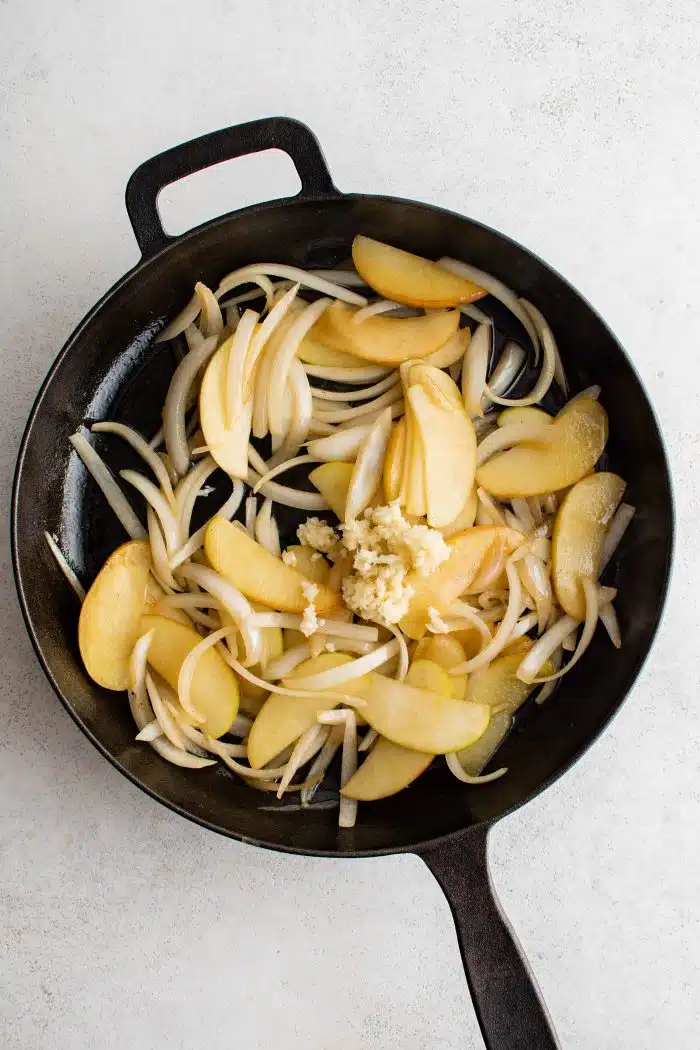 Minced garlic added to a large cast iron skillet filled with cooking onions and apples.
