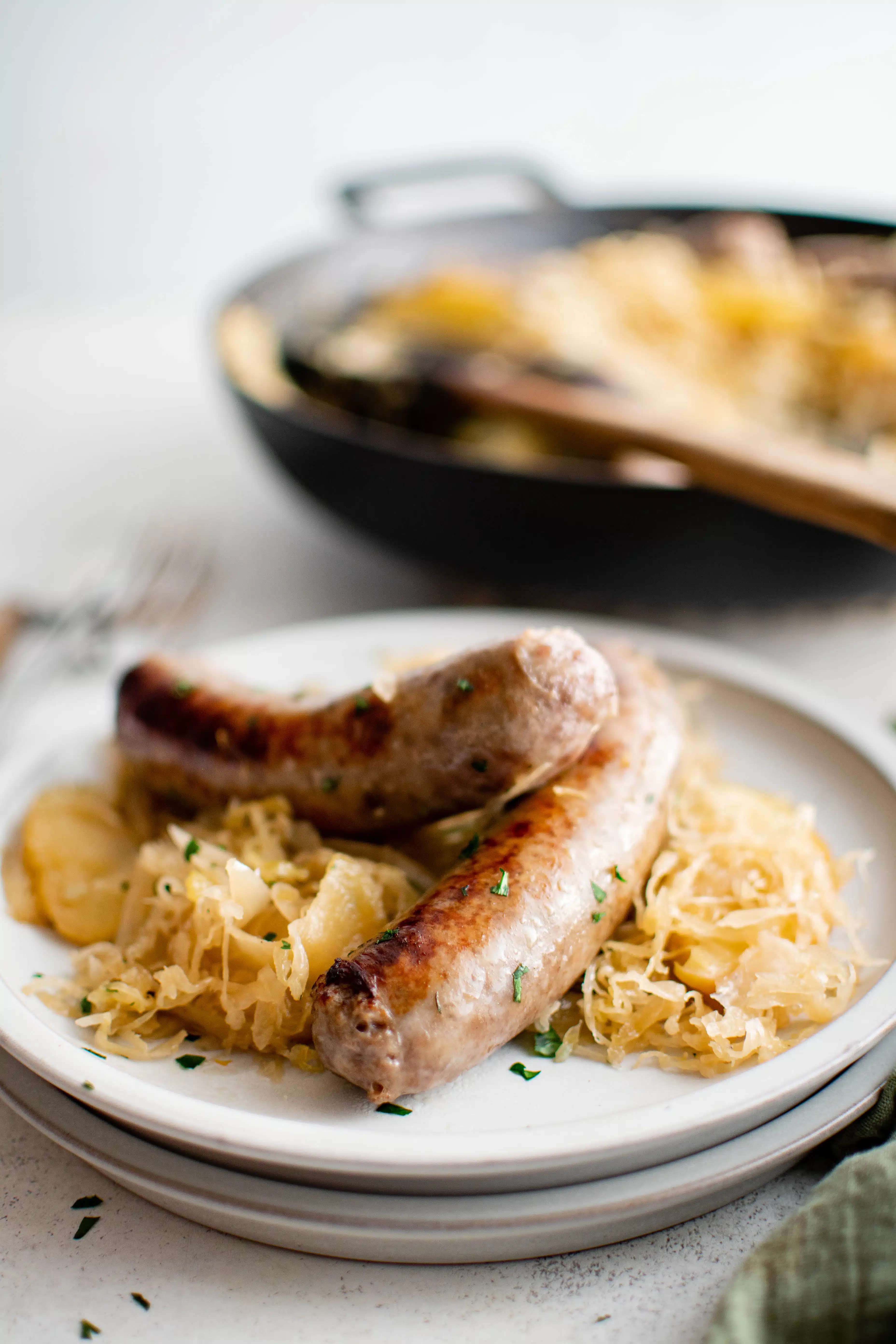 Two juicy bratwurst nestled on top of a pile of sauerkraut sauteed and mixed together with apples and onions on a white plate.