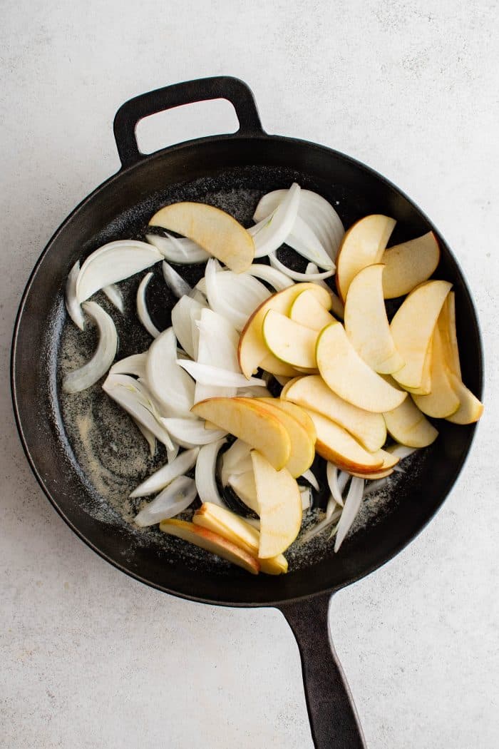 Sliced onions and apples cooking in a large cast iron skillet.