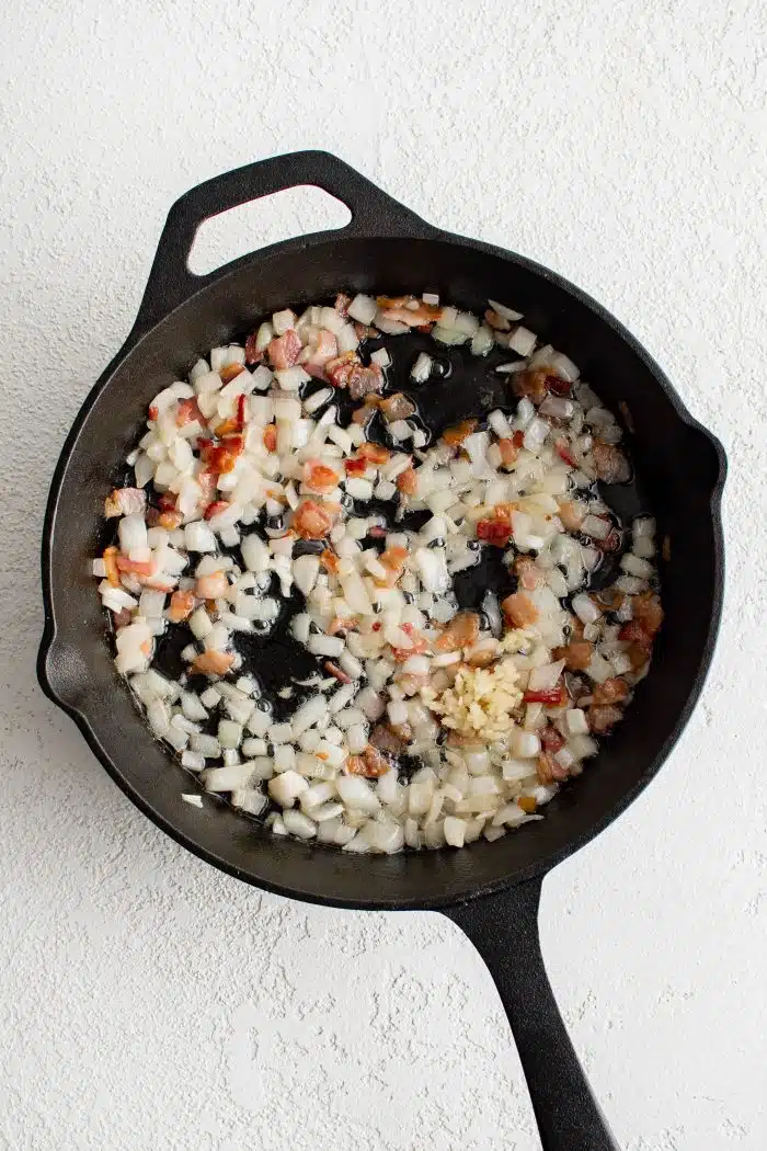 Chopped bacon and onion cooking in a large cast iron skillet.