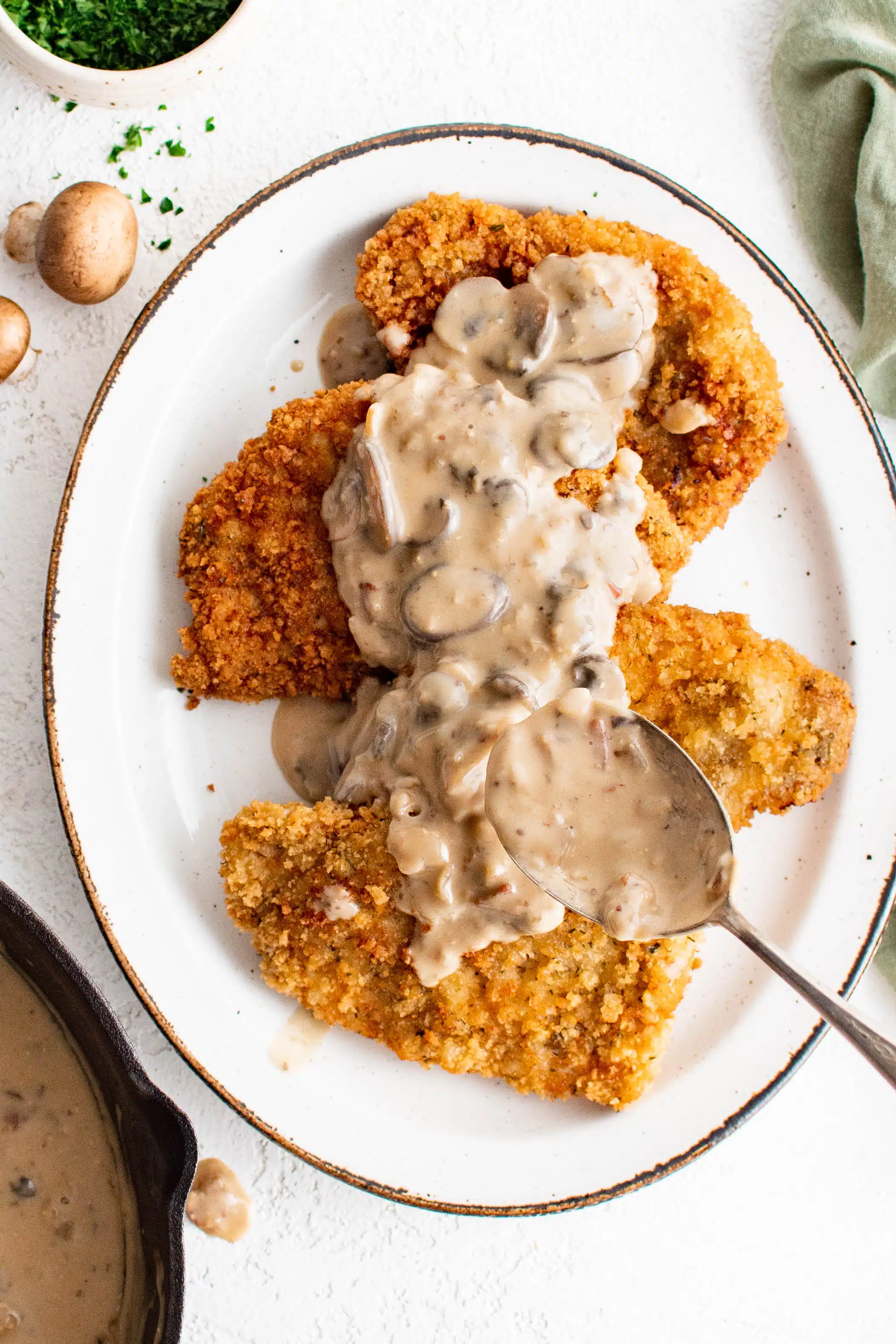 Large spoon carefully spooning mushroom sauce over four breaded and fried pork cutlets.