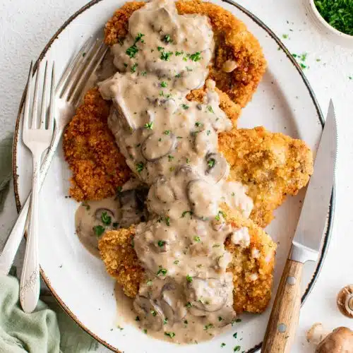 Large platter filled with four breaded and fried pork cutlets smothered in a bacon mushroom cream sauce and garnished with freshly minced parsley.