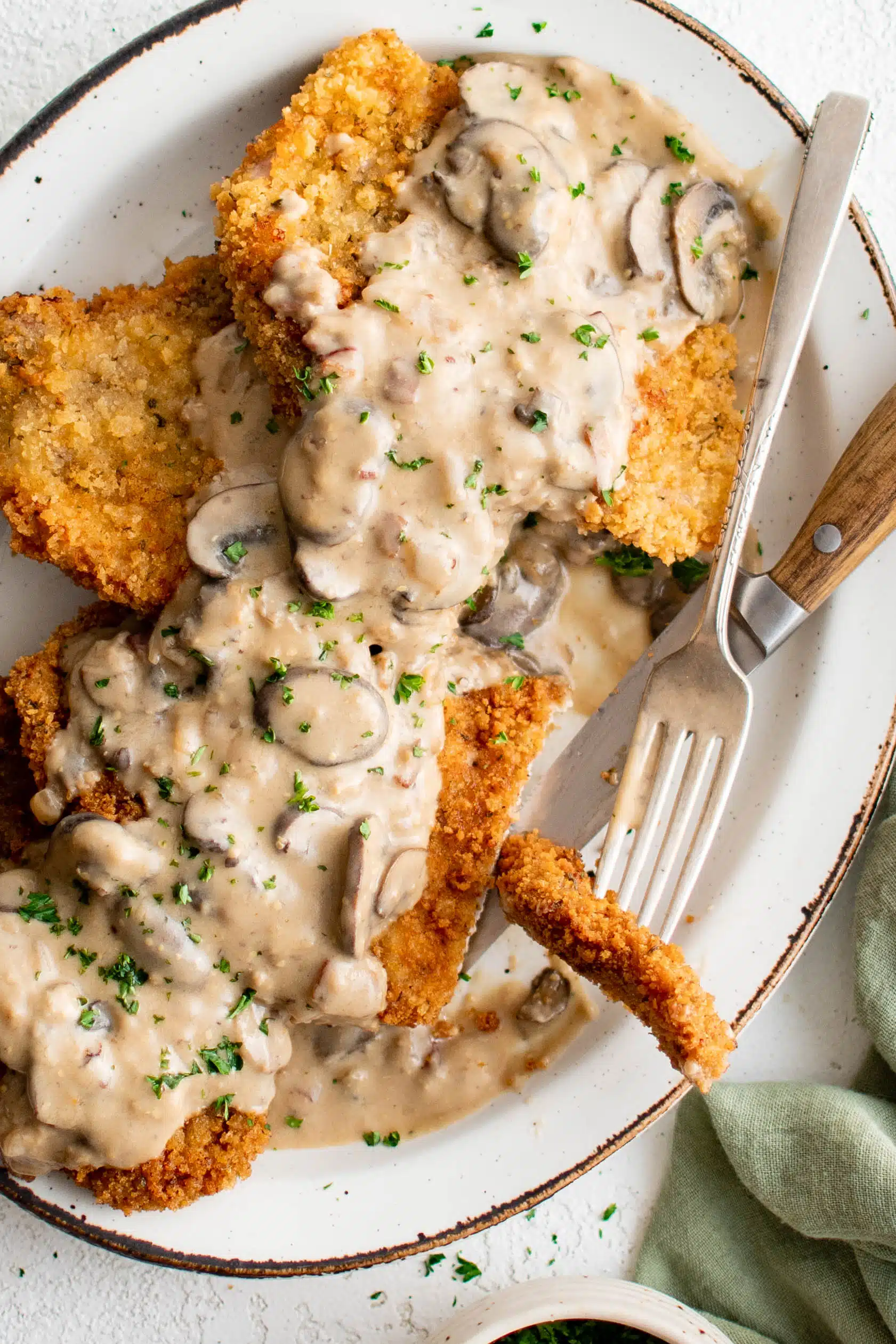 Large platter filled with four breaded and fried pork cutlets smothered in a bacon mushroom cream sauce and garnished with freshly minced parsley.